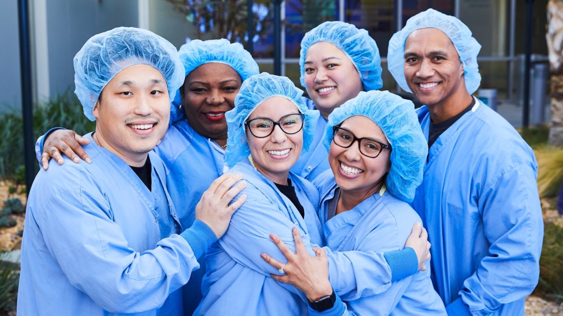 Group of six surgical techs wearing blue scrubs and smiling